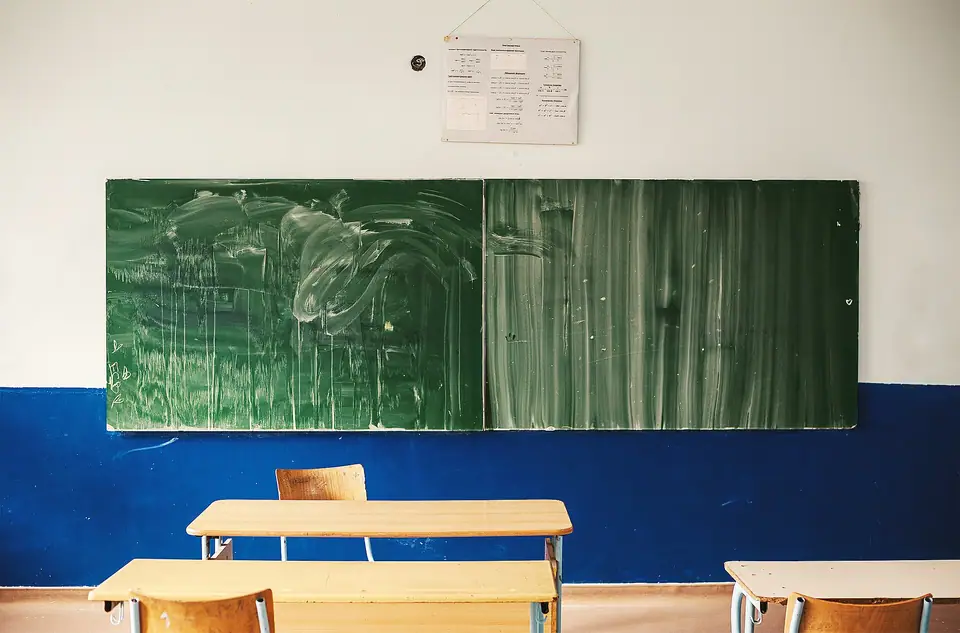 Silinmiş yeşil yazı tahtasının önünde boş ahşap sıralar ve sandalyeler