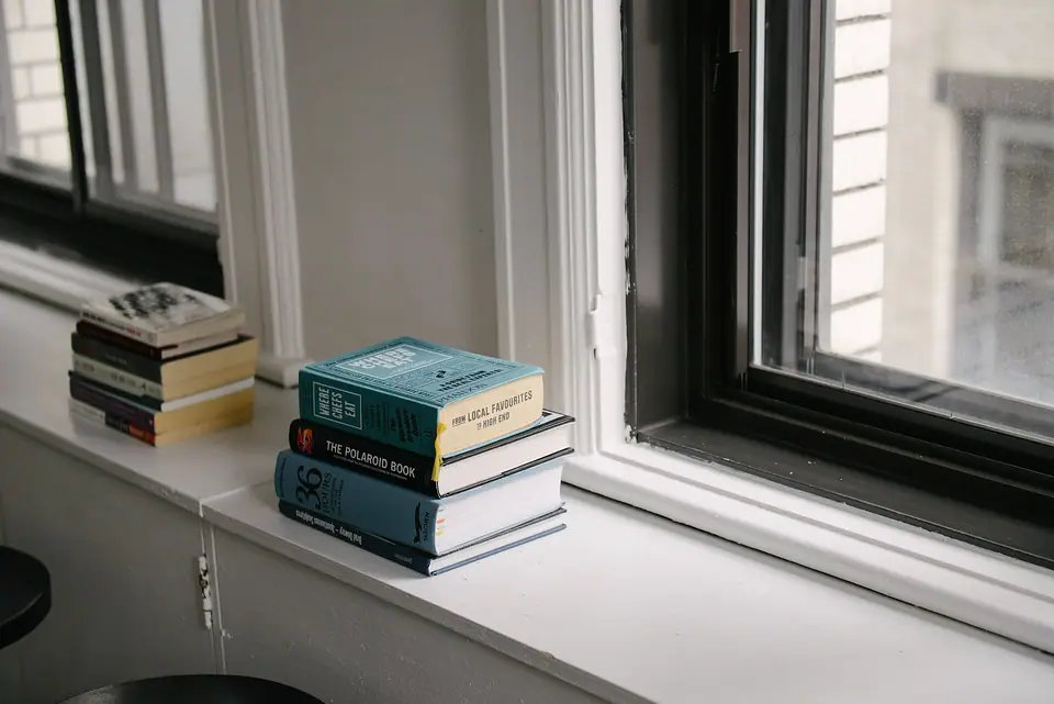 Pencere kenarında üst üste duran iki küçük kitap yığını