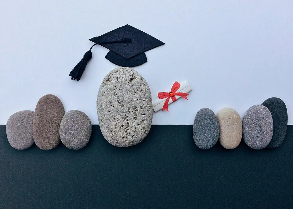 Taşlardan oluşan bir dizide ortadaki büyük taşın üzerinde mezuniyet kepi ve kurdeleli diploma rulosu